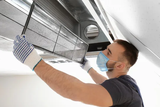 Technician removing an air return filter grille from a ceiling